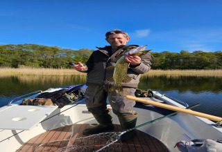 Man fishing on a boat at LAWENDA holiday cottage in Grąbczyn, Denmark, proudly holds up a caught fish.