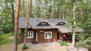 Træhytte kendt som Holiday home Debki omgivet af en tæt skov, set udefra på en rolig dag.