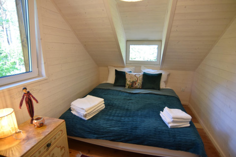 Et hyggeligt soveværelse i træ med en dobbeltseng, grønne puder og håndklæder, Holiday home «Debki», Sverige.