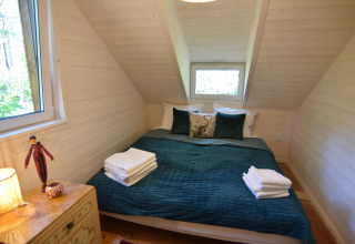Et hyggeligt soveværelse i træ med en dobbeltseng, grønne puder og håndklæder, Holiday home «Debki», Sverige.