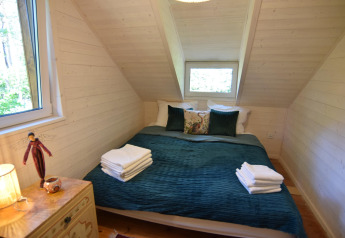 Acogedor dormitorio de madera con cama doble, cojines verdes y toallas en Holiday home «Debki», Suecia.