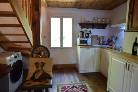 Cuisine chaleureuse dans un gîte suédois, plafond en bois, machine à laver et chaise avec coussin chien.
