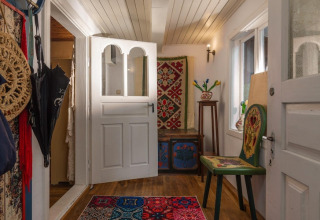 Entrée chaleureuse d’une maison de vacances suédoise avec meubles peints et tapis coloré au sol.