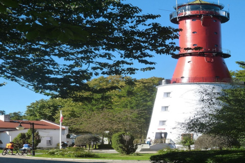 Photo d'une maison de vacances à côté d'un phare rouge et blanc emblématique entouré d'arbres verts.