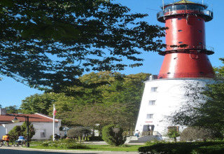 Photo d'une maison de vacances à côté d'un phare rouge et blanc emblématique entouré d'arbres verts.