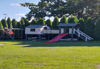 Parque infantil en casa de vacaciones en Świnoujście con tobogán, columpios y casita, rodeado de árboles.