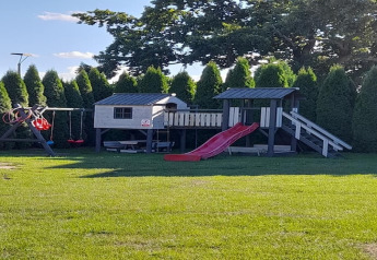 Parque infantil en casa de vacaciones en Świnoujście con tobogán, columpios y casita, rodeado de árboles.