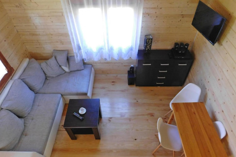 Luminoso soggiorno in baita con pareti in legno, divano angolare, tavolino, TV e angolo pranzo per cinque.