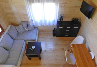 Sala luminosa en una cabaña con sofá en L, mesa de centro, televisor, cómoda y comedor para cinco personas.