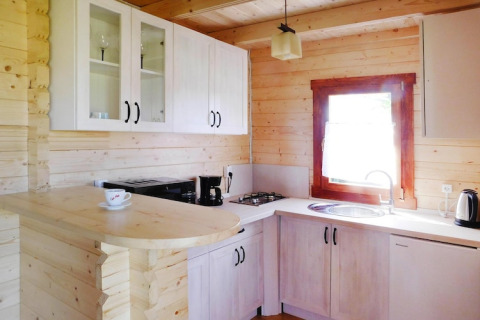 Cocina de madera luminosa en cabaña de vacaciones con armarios blancos, fregadero y ventana soleada.