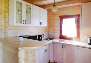 Cocina de madera luminosa en cabaña de vacaciones con armarios blancos, fregadero y ventana soleada.