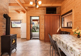 Knusse lodge met houten interieur, kachel, eettafel, kast en zicht op de buitenruimte.