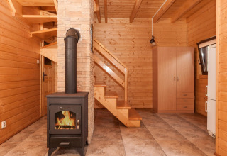 Interieur van een houten lodge met houtkachel, trap, kledingkast en tegelvloer in een vakantiecomplex.