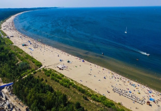 Luchtfoto van een lang zandstrand met blauwe zee, groene bossen en veel mensen op het strand.