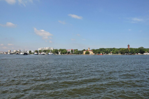Vista sobre el agua mirando edificios y árboles en la orilla con cielo azul en Swinoujście, Alemania.
