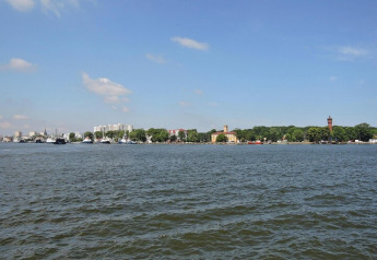 Vista sull'acqua verso edifici e alberi sulla riva sotto un cielo azzurro a Swinoujście, Germania.