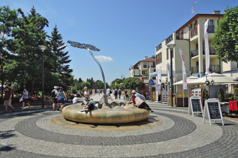 Vista urbana junto a casas de vacaciones en Swinoujście con personas disfrutando de una fuente moderna.