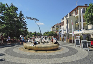 Vista urbana junto a casas de vacaciones en Swinoujście con personas disfrutando de una fuente moderna.