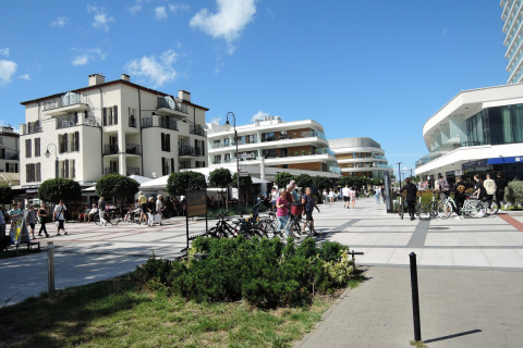 Calle peatonal animada con edificios modernos y clásicos, personas paseando y bicicletas a la vista.