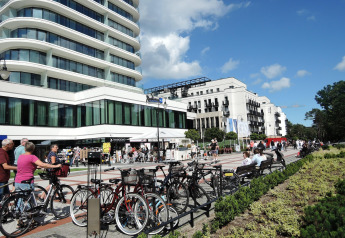 Street scene with modern buildings, bicycles, and people in Swinoujście under a clear blue sky.
