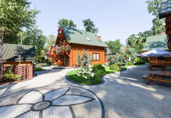 Vakantiecomplex met houten chalets, groene daken, bloemenperken en betegelde paden tussen de bomen.