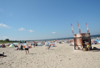 Drukke strand met kleurrijke tenten, mensen en een kleine koffiebar onder een heldere blauwe lucht.