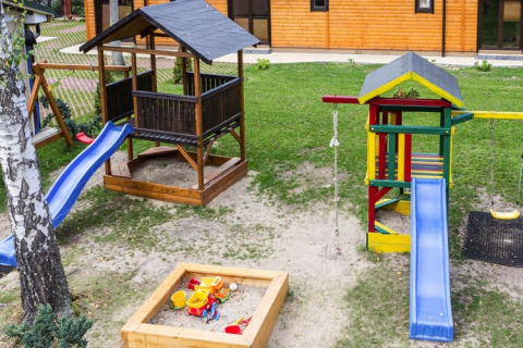 Playground with slides, swings, and sandbox near a wooden house at Holiday complex Pobierowo-Doppelhaus 4 and 2.