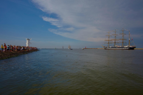 Mensen verzamelen zich bij het water en kijken naar een groot zeilschip bij een witte molen in Swinoujście, Duitsland.
