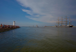 Mensen verzamelen zich bij het water en kijken naar een groot zeilschip bij een witte molen in Swinoujście, Duitsland.