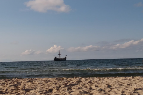 Zandstrand met een schip op de zee aan de horizon, blauwe lucht en enkele lichte wolken erboven.