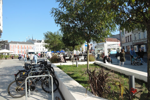 Stedelijk plein in Swinoujście met fietsen, bomen en mensen op een zonnige dag in het centrum.
