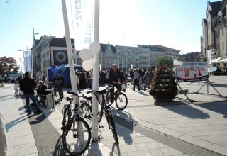En livlig plads i Świnoujście med cykler, mennesker, valgplakater og byens bygninger i baggrunden.