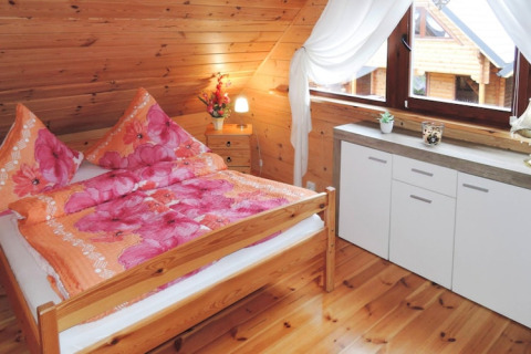 Knusse slaapkamer met houten wanden, tweepersoonsbed en grote ramen in een huis in Rewal, Duitsland.