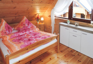Knusse slaapkamer met houten wanden, tweepersoonsbed en grote ramen in een huis in Rewal, Duitsland.