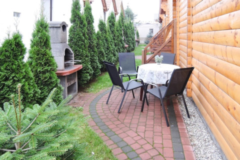 Buitenpatio bij een lodge in Rewal met tafel, vier stoelen, barbecue en groene heg langs het pad.