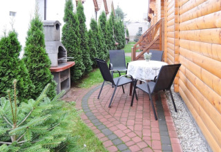 Buitenpatio bij een lodge in Rewal met tafel, vier stoelen, barbecue en groene heg langs het pad.
