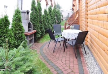 Udendørs terrasse ved en hytte med bord, fire stole, grill og grønne planter langs stien i Rewal.