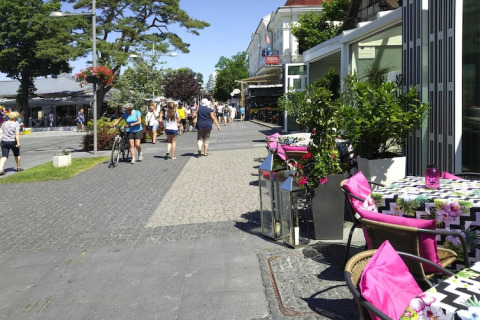 Udendørs café med farverige puder og blomster i solen, folk går på gågade nær Rewal, Tyskland.