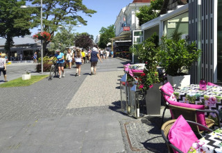 Udendørs café med farverige puder og blomster i solen, folk går på gågade nær Rewal, Tyskland.