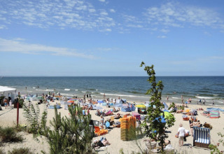 Drukbezochte strand in Rewal met mensen, strandstoelen en uitzicht op zee nabij comfortabele vakantiewoningen.