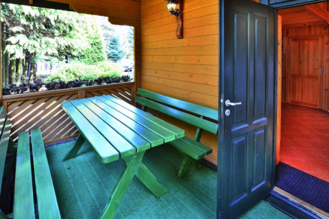 Udendørs spisested med grøn bænk og bord på en overdækket terrasse i feriebolig nær skov i Kołobrzeg.