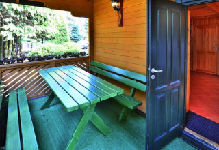 Udendørs spisested med grøn bænk og bord på en overdækket terrasse i feriebolig nær skov i Kołobrzeg.