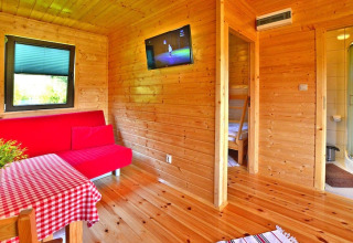 Innenaufnahme eines Holzferienhauses mit rotem Sofa, Esstisch und Blick ins Bad und Schlafzimmer.
