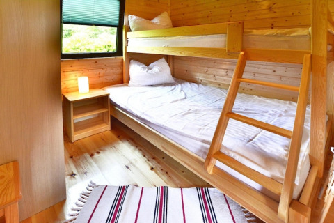 Gezellige houten kamer met stapelbed, nachtkastje, lamp en raam in een zomerhuisje voor 4 personen.