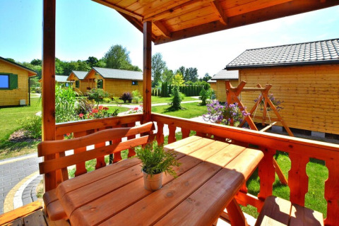 Terraza de madera con mesa y bancos, rodeada de jardines y cabañas de verano para 4 personas en Mielno.