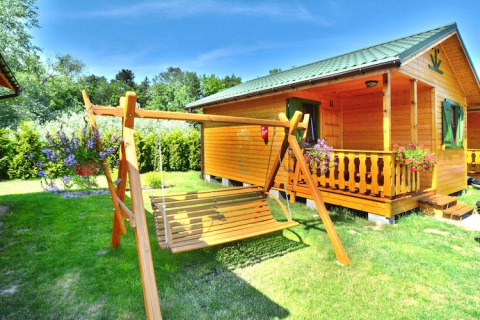 Zomerhuisje voor 4 personen in Mielno met houten schommelbank, bloemen en groene tuin onder blauwe lucht.