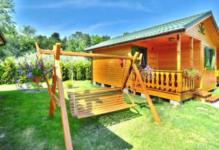 Cabaña de verano para 4 personas en Mielno con columpio de madera, porche, flores y jardín verde soleado.