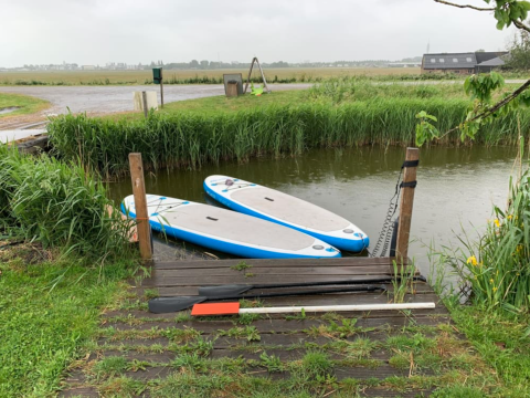 Twee paddleboards liggen aangemeerd aan een kleine houten steiger bij Boerencamping Swarthoeve, Noord-Holland.