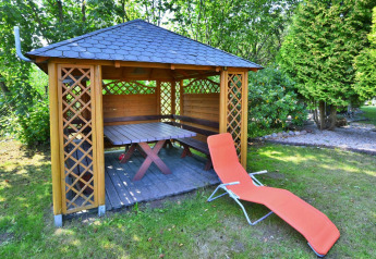Pérgola de madera con mesa, banco y tumbona naranja en el jardín de una casa vacacional para 6 en Kołobrzeg.