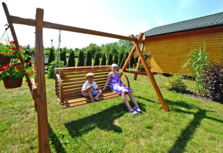Twee kinderen zitten op een houten schommel bij een huisje bij ‘Summer cottages for 4 people Mielno’ in Denemarken.